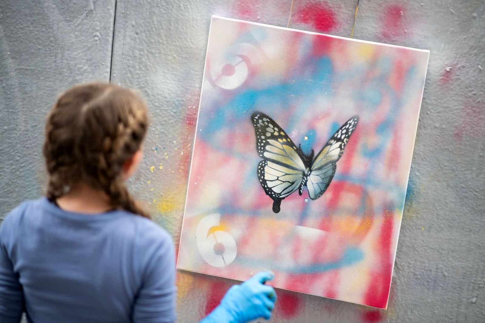 A young visitor spray-painting a butterfly stencil during Art Week 2025